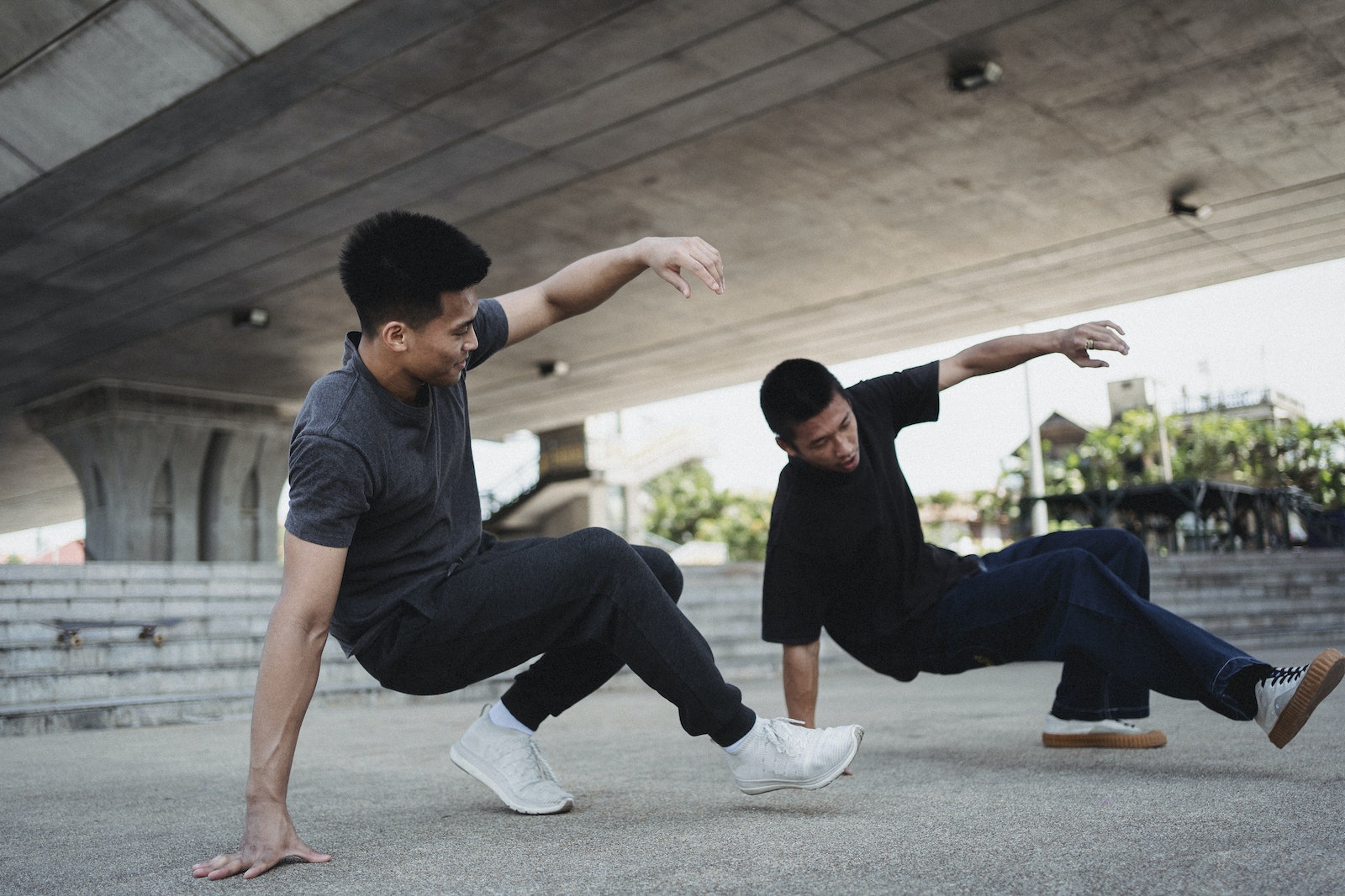 Side view full length sporty Asian men in activewear performing street style dance under urban elevated highway