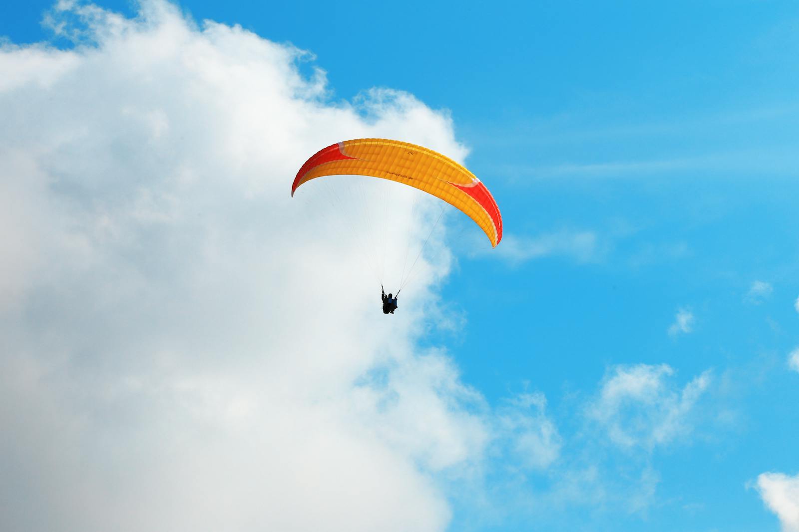 A thrilling paragliding experience captured against a vivid blue sky with clouds.